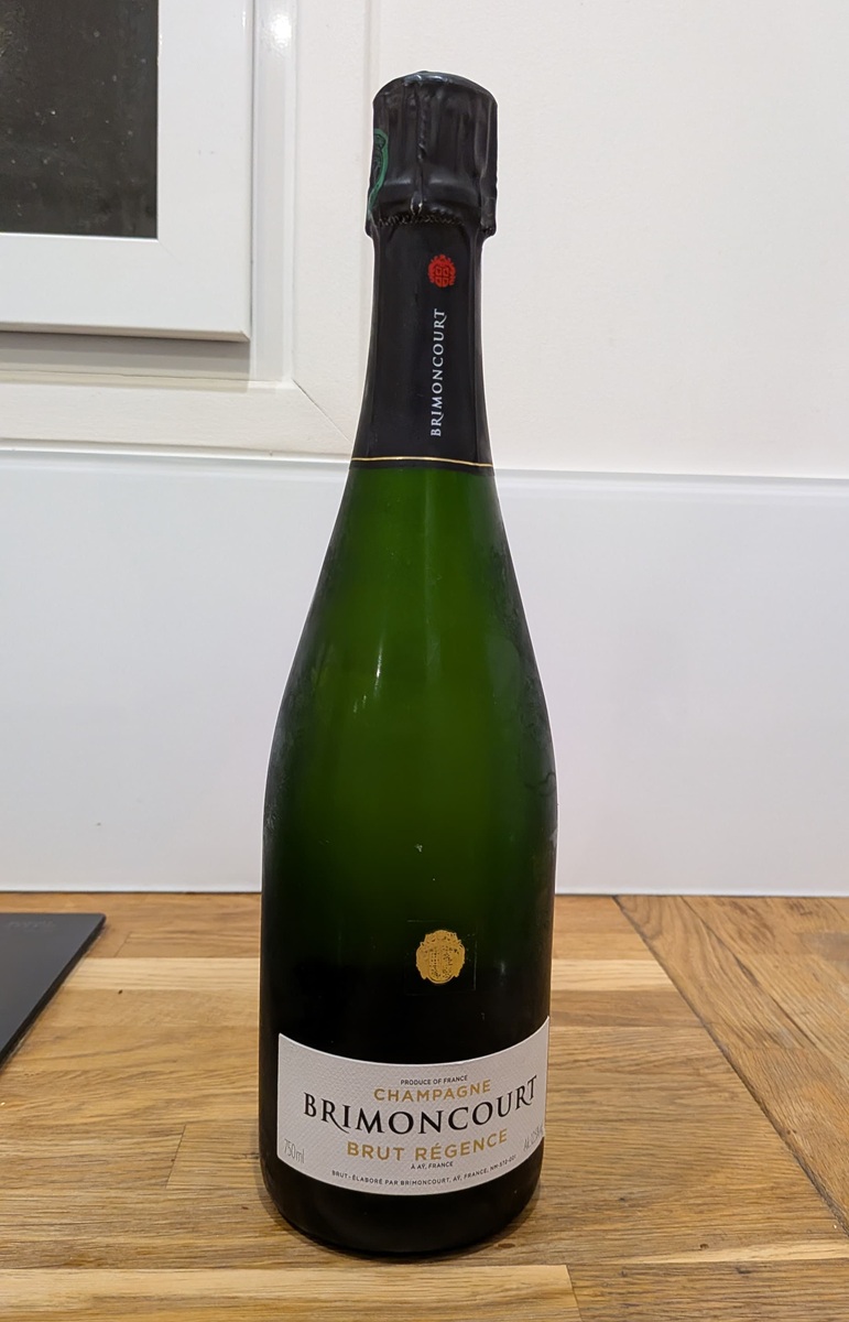 Photo de bouteille de champagne prise au smartphone avant traitement, posée sur une table avec reflets et objets autour